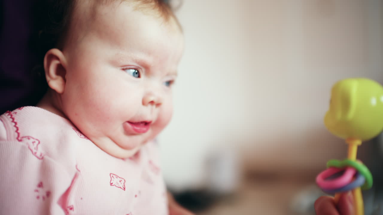 Glad baby som smiler og reagerer på fargerikt leketøy under lek