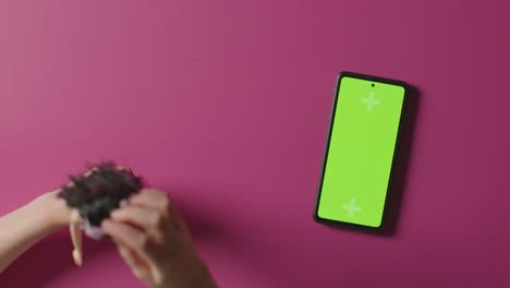 overhead shot of girl playing with toy doll next to green screen mobile phone