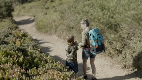 woman with backpack holding child's hand walking down dirt road