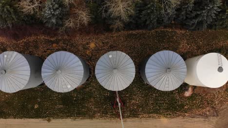 Imágenes-De-Drones-Superiores-De-Grandes-Contenedores-De-Granos-De-Metal-En-La-Zona-Rural-De-Alberta-Con-El-Sol-Bajo-Acechando-Entre-Contenedores-Redondos