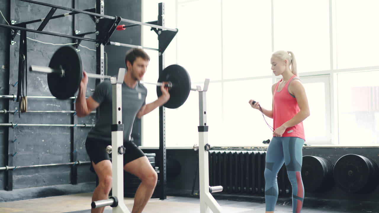Man doing barbell squats with a personal trainer