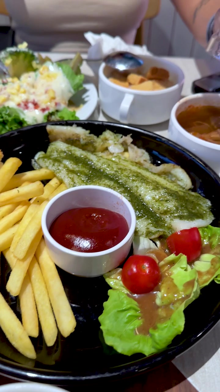 Vista ravvicinata rotante di un trancio di pesce, patatine fritte, insalata e zuppa sotto la calda illuminazione di un ristorante.