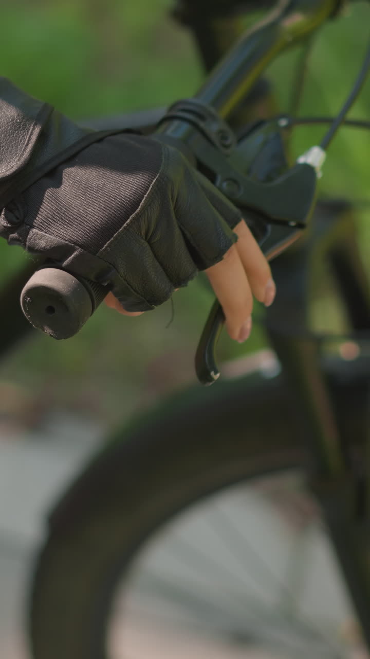 primer plano del manillar de la bicicleta individual con la mano con guante, acelerando y sosteniendo la palanca del freno con precisión, la luz del sol se refleja sutilmente en el guante de cuero, el fondo presenta un desenfoque de vegetación