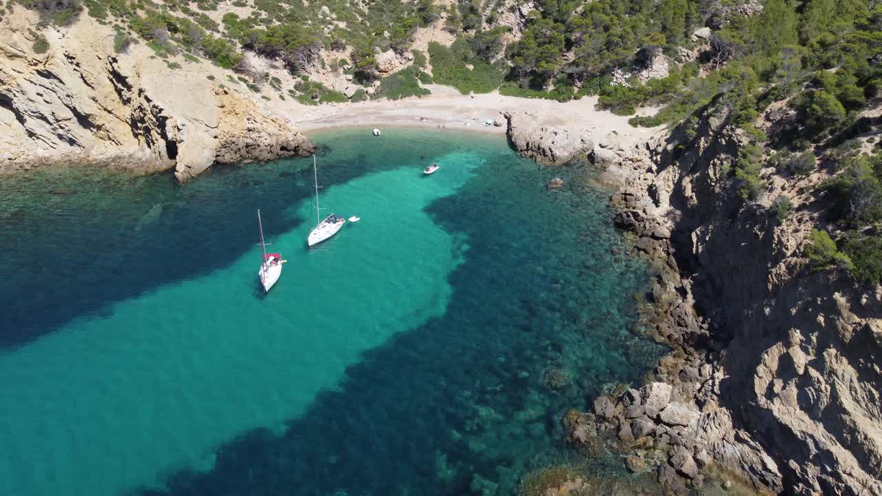 Luftfoto af en strand med turkis og krystalklart vand og ankerliggende både på Mallorca, Balearerne