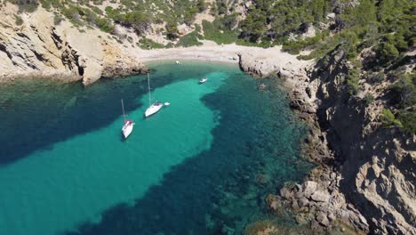 aerial view of a beach with turquoise and crystal clear water with anchored boats in majorca, balearic islands