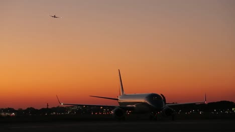 avión en la pista de aterrizaje al anochecer con otra silueta de jet en el cielo