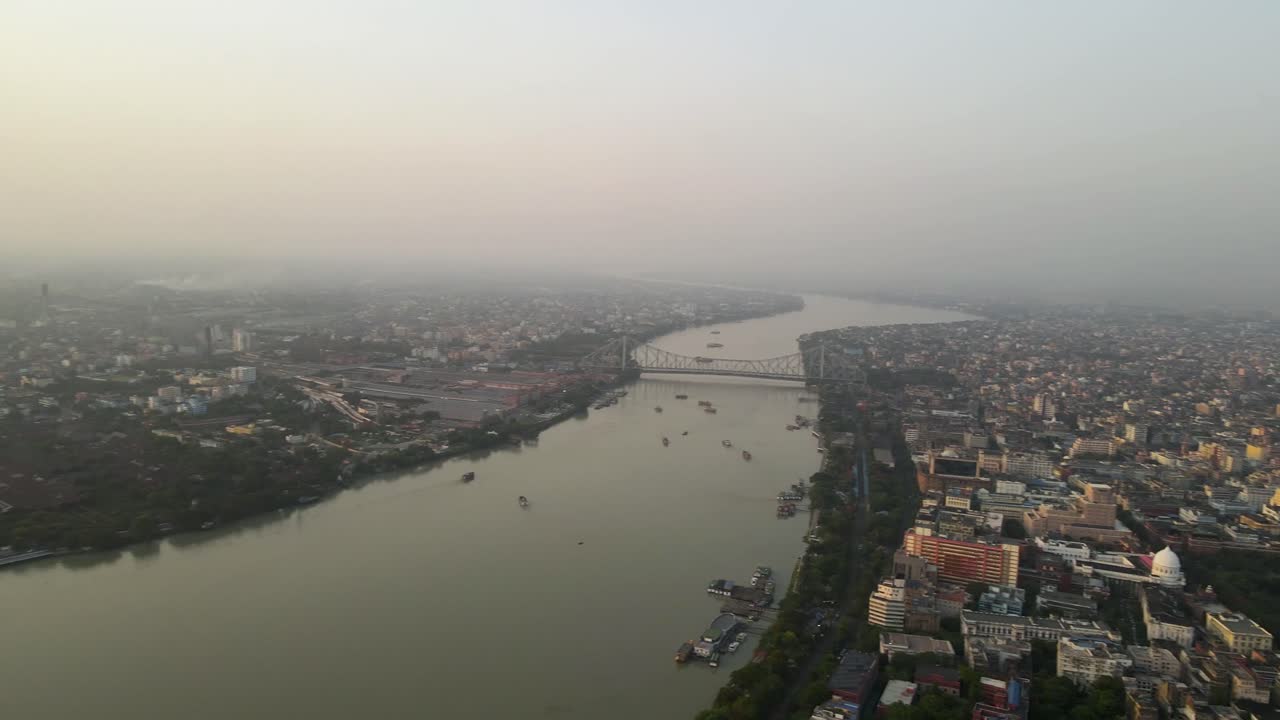 Breathtaking aerial drone shot of the Howrah Bridge, reflecting on the tranquil Hooghly River at dusk.
