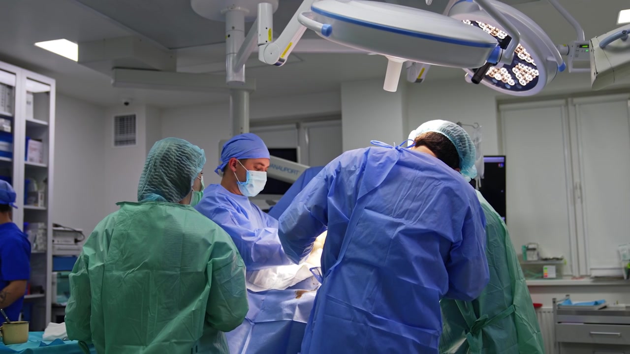 Professional healthcare team cooperating at modern surgery. Surgeons operate trauma assisted by female scrub nurse.