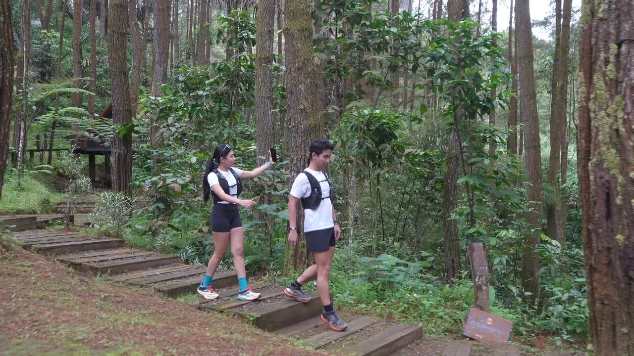 Indonesian couple on forest trail run with woman recording video on smartphone