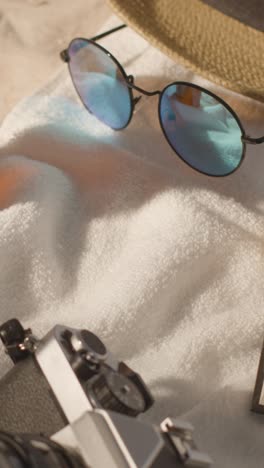 Vertical-Video-Summer-Holiday-Concept-Of-Sunglasses-Sun-Hat-And-Camera-On-Beach-Towel-On-Sand