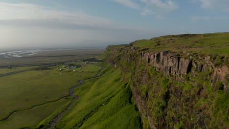 Birds-eye-flying-toward-breathtaking-Seljalandsfoss-waterfall,-the-most-famous-cascade-in-Iceland.-Drone-point-of-view-of-amazing-icelandic-landscape-over-mossy-cliffs-and-majestic-waterfall