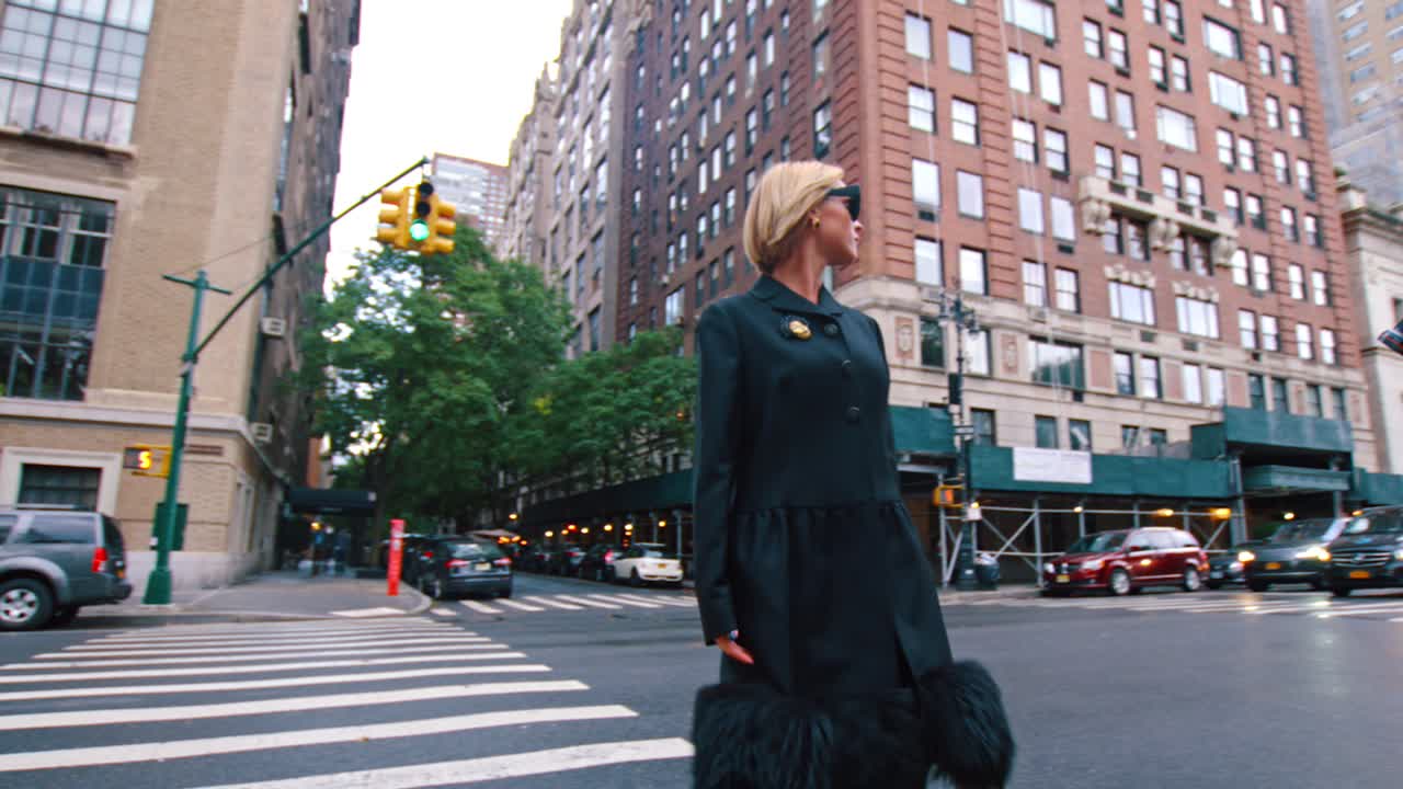 New York, USA, 9 October 2025: Fashion model crossing the street in New York City. Woman in long dark coat standing on zebra crosswalk at urban intersection with traffic lights