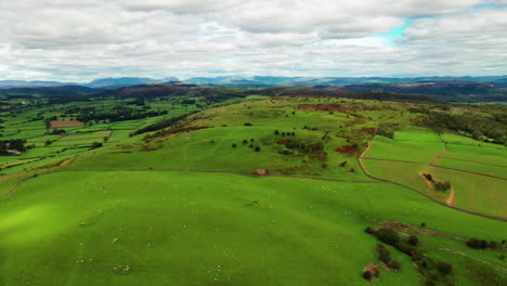 Tiro-Aéreo-Con-Vistas-A-Las-Verdes-Colinas-Y-Tierras-De-Cultivo-En-El-Distrito-Inglés-De-Los-Lagos,-Luz-Brillante-Con-Nubes-Blancas