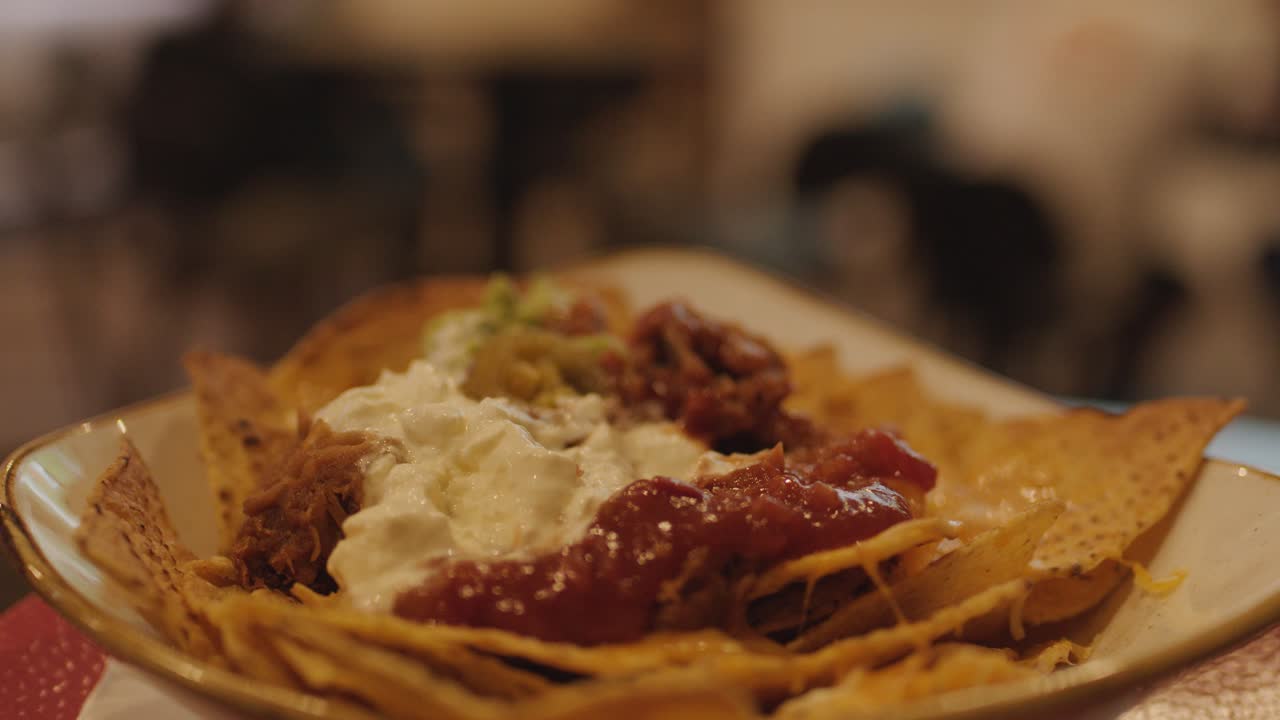Primo piano di nachos con salsa, panna e carne, mano che intinge una patatina, illuminazione calda da bar