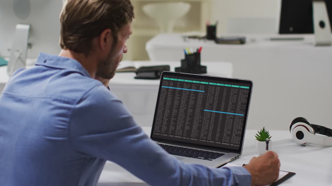 uomo caucasico seduto a scrivania a elaborare sul portatile e a prendere appunti