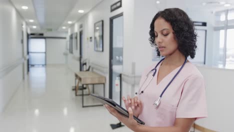 Focused-biracial-female-doctor-using-tablet-in-hospital-in-slow-motion