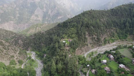 Aerial-footage-of-a-lush-valley-with-scattered-houses,-winding-roads,-and-a-river-flowing-through