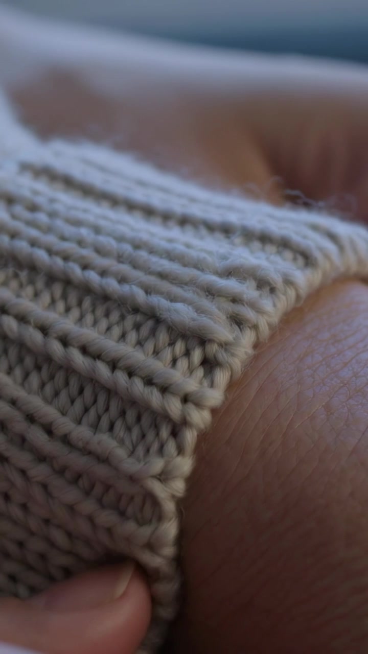Video verticale: Mani che afferrano e tirano un polsino a coste beige sul polso a casa per lisciare la maglia.