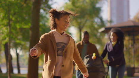 Happy-daughter-parents-walking-sunny-green-park-together.-Couple-push-stroller.