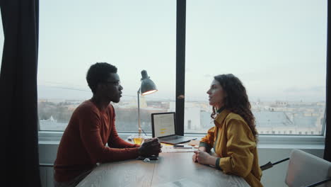 multiethnic coworkers talking at desk in rooftop office