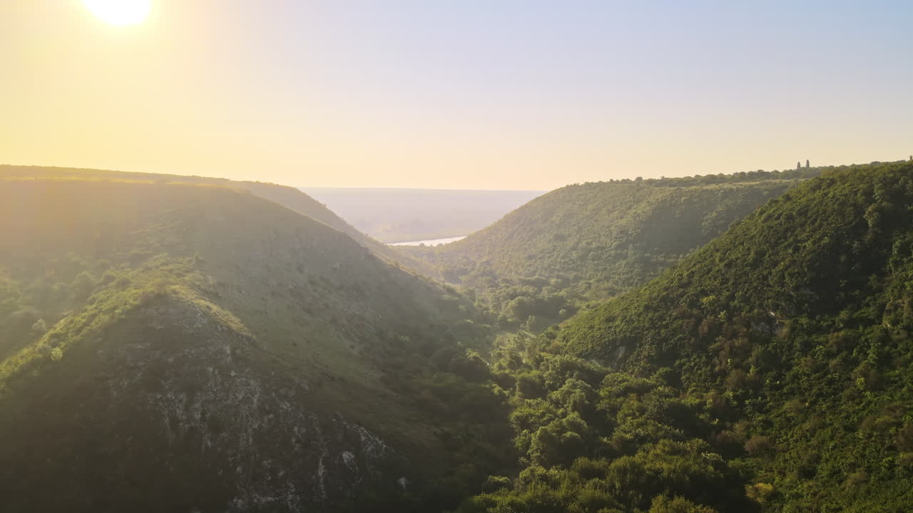 Aerial drone view of a valley with hill slopes covered with lush greenery, water in the distance, Moldova