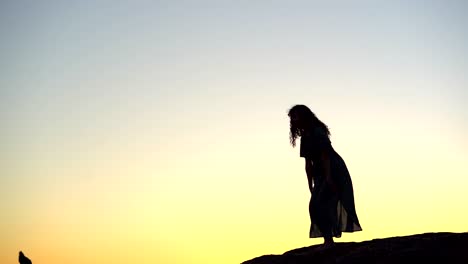 female silhouette walking on rocky hilltop at picturesque sunset