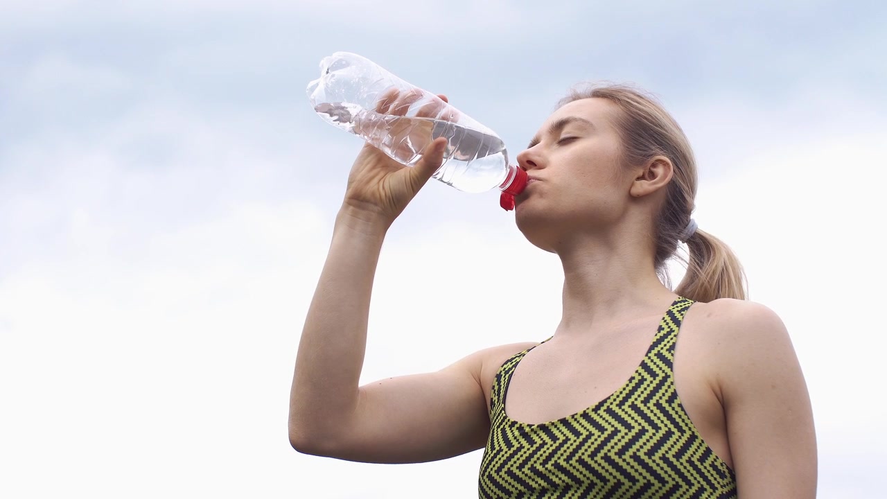 Giovane donna che beve acqua da una bottiglia all'aperto