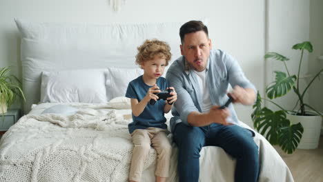 father and son playing video games on a bed