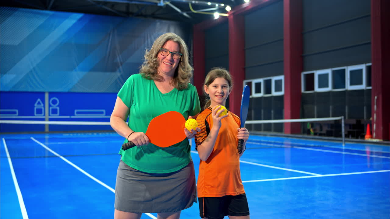A woman posing with her daughter after playing pickleball on a blue, inside court