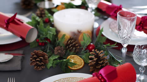 Close-in-tilt-shot-of-a-Christmas-dinner-table-with-seasonal-decorations,-crystal-glasses-and-Christmas-crackers-on-plates