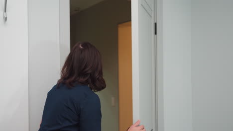 skin therapist in navy uniform opens door with friendly gesture and speaks to client waiting behind door in bright white treatment room, conveying professional, welcoming interaction before facial