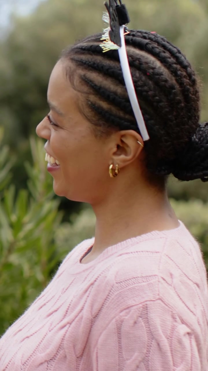 Vertical video: Hands reaching placing tiara on woman in pink knit braids to secure fit in park