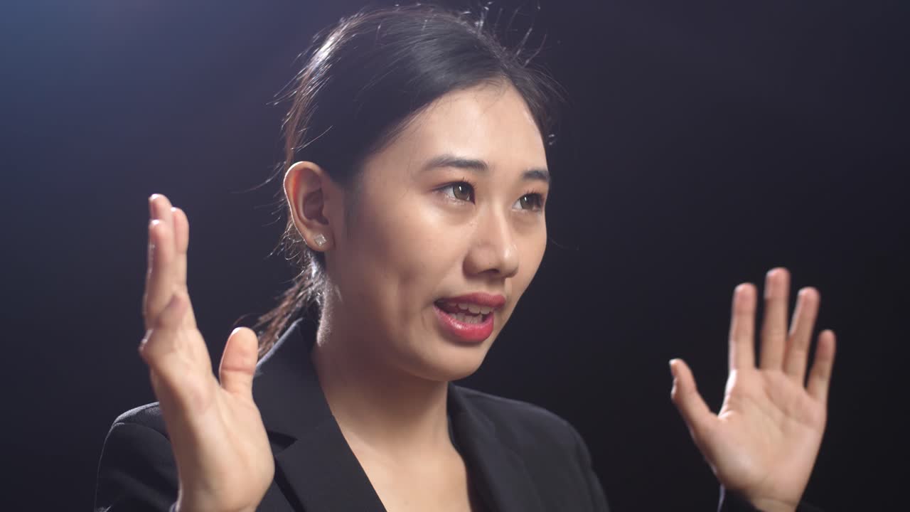 블랙 스크린 스튜디오에서 말하는 비즈니스 슈트를 입은 아시아 스피커 여성의 측면 시각