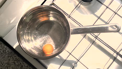 an egg boils in water in a saucepan on a gas stove, dutch angle