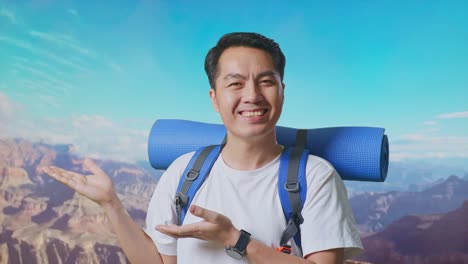 close up of asian male hiker with mountaineering backpack smiling and pointing to side while traveling at the top of mountain