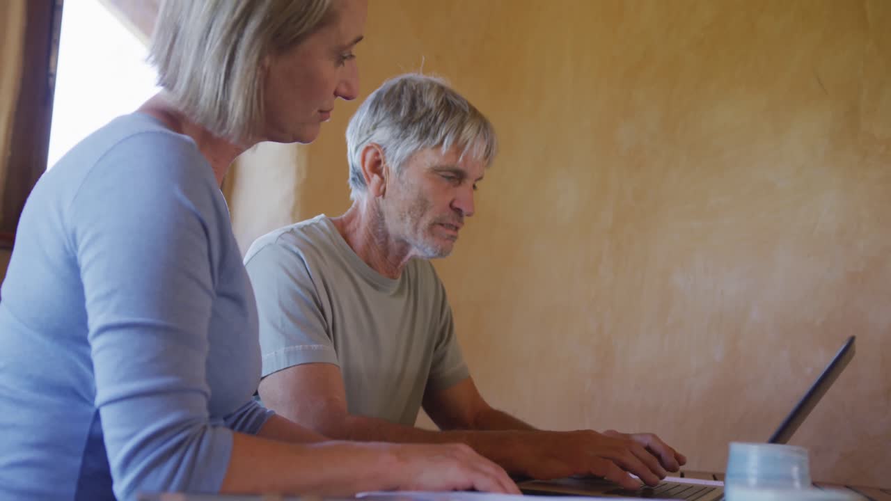 Senior caucasian couple using laptop and sitting at table