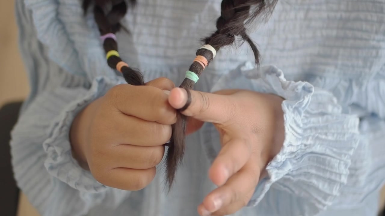 三つ編みのおさげ髪にカラフルなヘアゴムで遊ぶ子供の手。