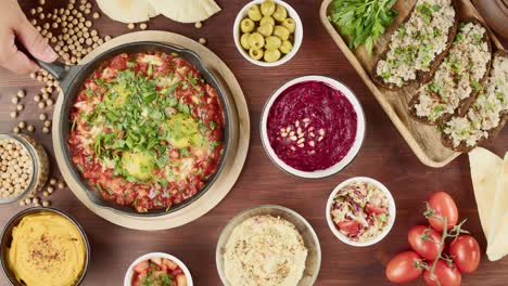 cocina tradicional israelí. shakshuka en sartén decorado con perejil, forshmak y hummus en la mesa. platos nacionales judíos vista superior. huevos fritos en salsa de tomate, salsa, pita, cultura de oriente medio
