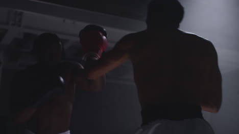 toma de cerca de dos boxeadores masculinos con guantes en el ring de boxeo luchando en un partido de boxes con iluminación de bajo nivel 1