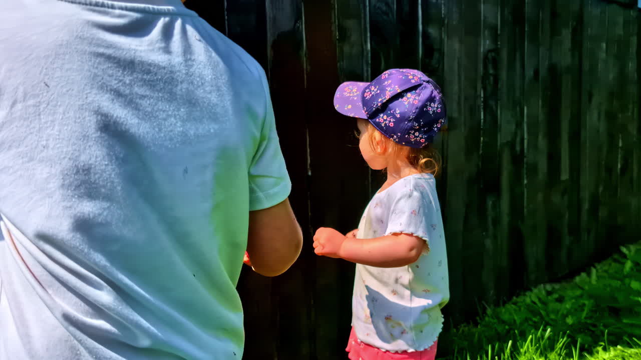 Children painting wooden fence outdoors with brushes on summer day teamwork fun