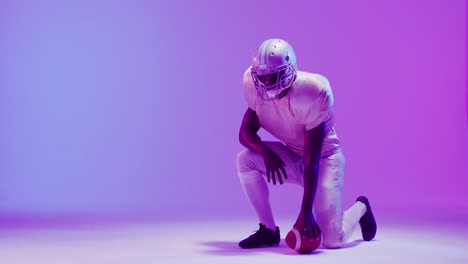 Video-of-african-american-american-football-player-with-ball-over-purple-neon-background