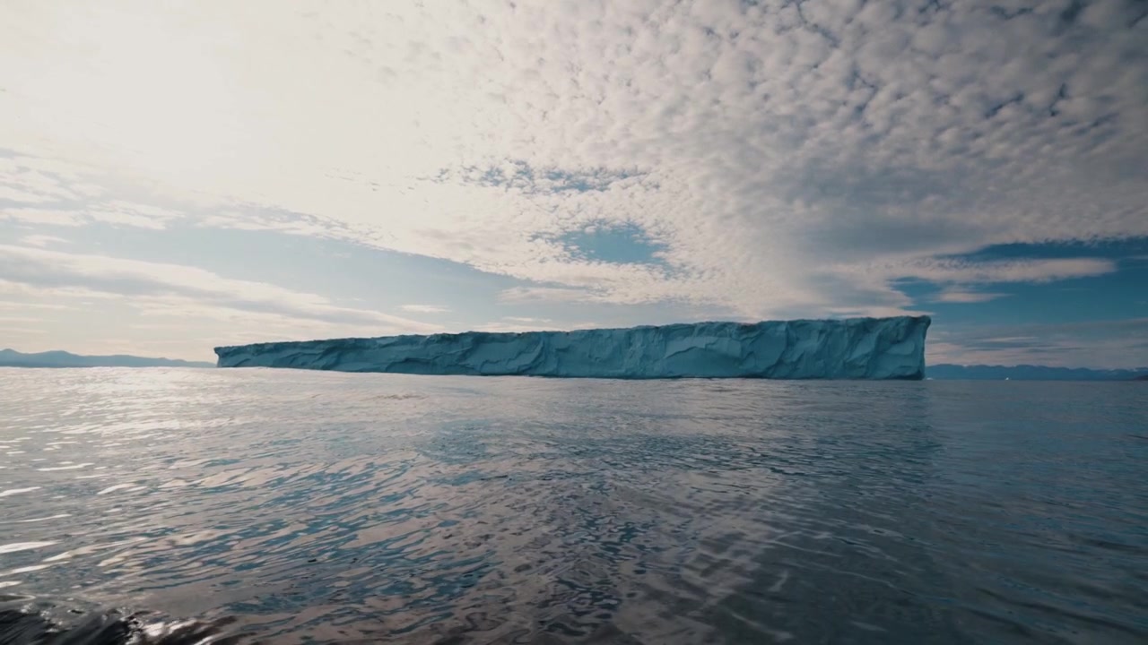 Tracking shot along a massive tabular iceberg floating in calm Arctic ocean waters.