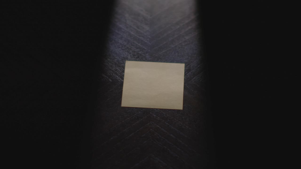 Slow motion close up footage of a hand writing out "F*CK YOU" on a paper note and placing it on a table. Shot in dramatic lighting for an impressive title or transition
