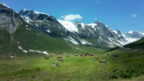 aerial dolly to cabins in green valleys and distant snowy mountains in norway, with a scenic road running through the landscape