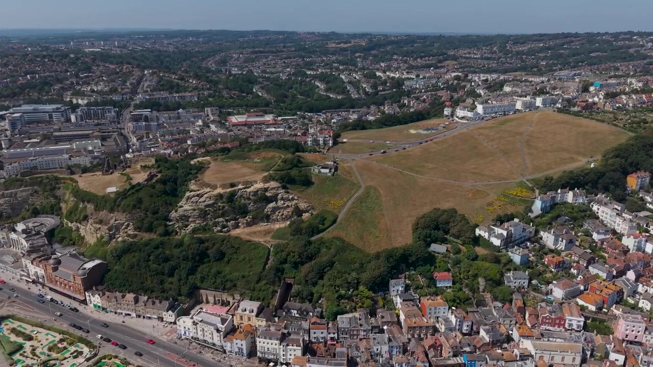 Dronebeeld van Hastings West Hill onthult het parklandschap van The Ladies Parlour en de ruïnes van Hastings Castle, met daken van de kustplaats en het omliggende landschap van East Sussex