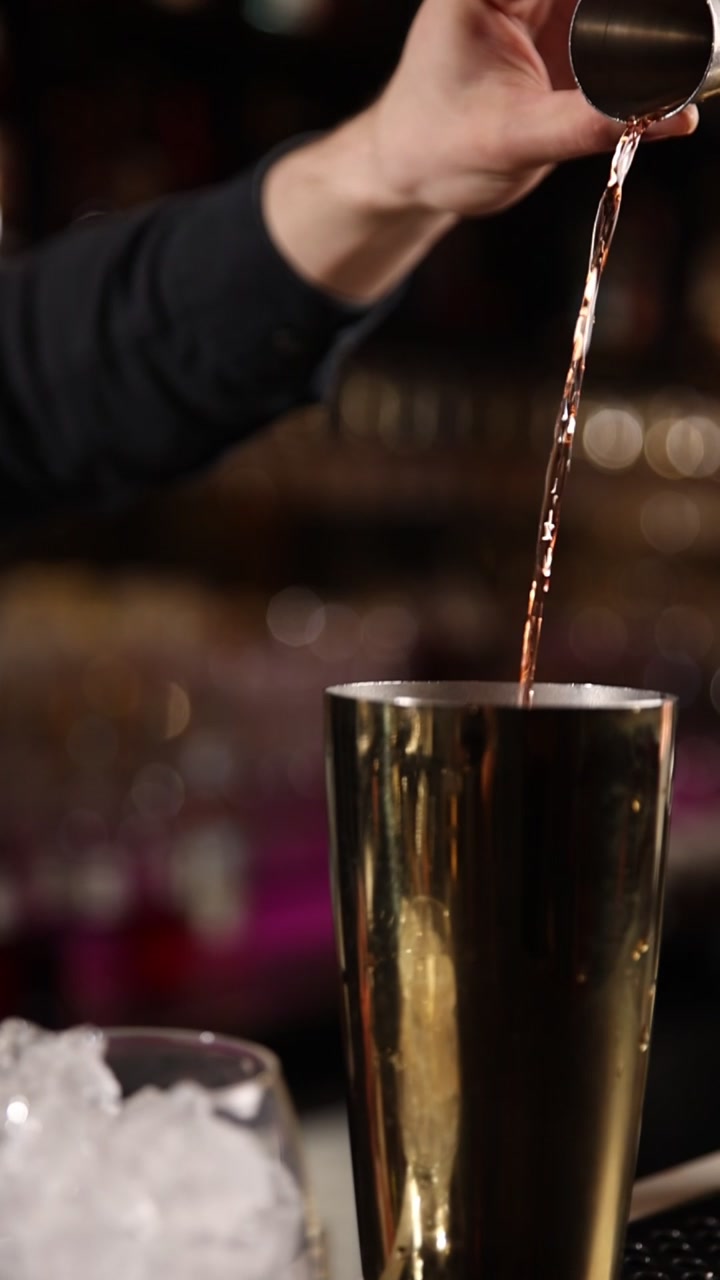 Barman che versa liquido ambrato da un jigger in uno shaker dorato