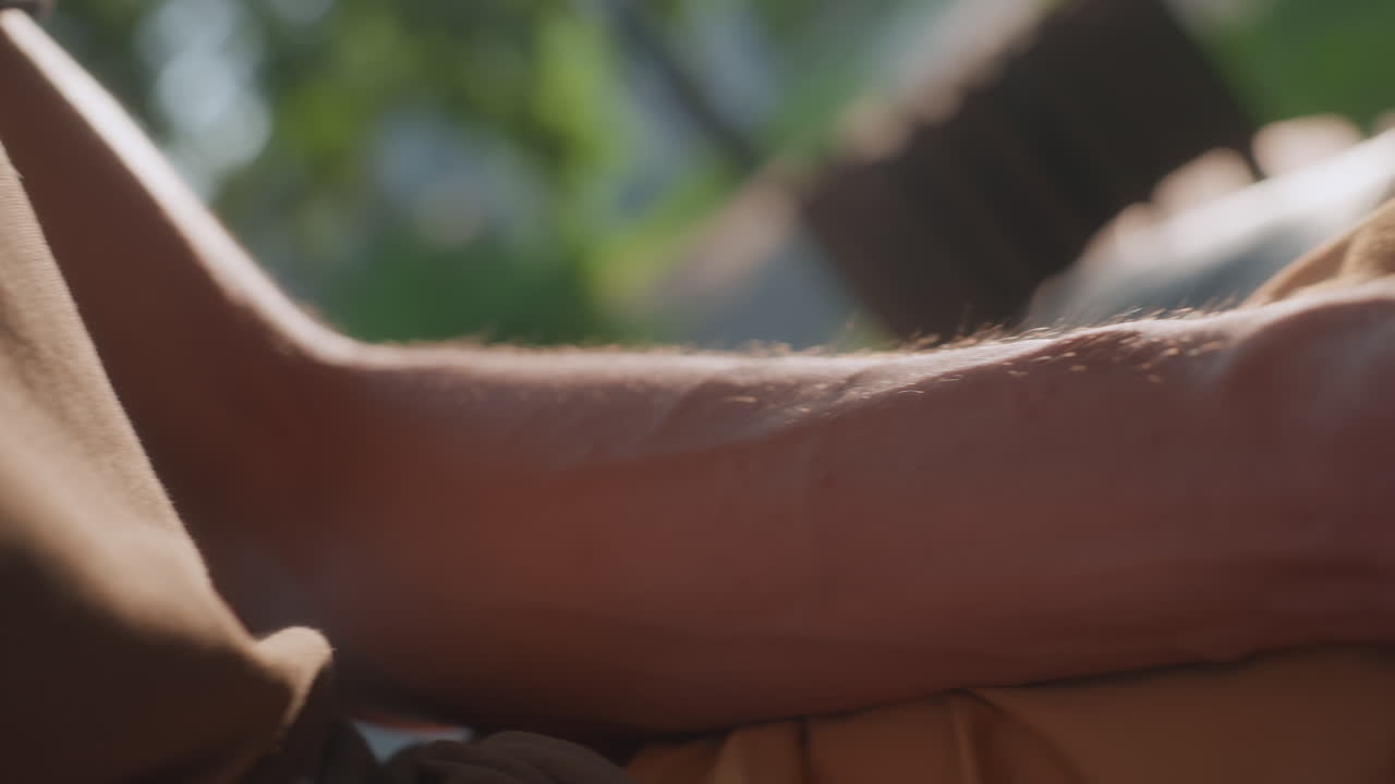 Close Shots Of Young ManS Chest, Collar And Hands Using Phone, Fingers Tapping Screen And Adjusting Grip, Soft Sunlight Through Trees Creates Reflective Glare On Device And Textured Fabric Of Shirt