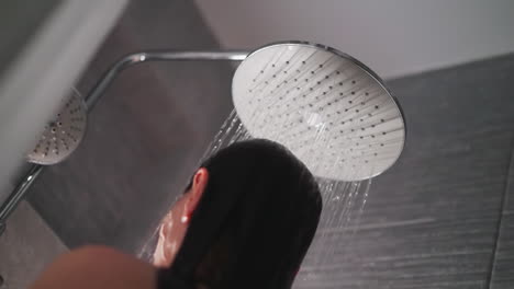 woman relaxes in warm embrace of water in shower. water falls on woman naked body in shower. young lady stands in shower in wash time in evening