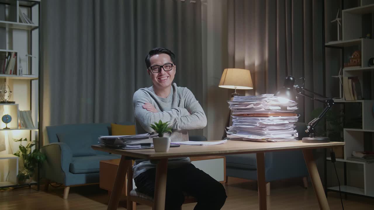 Asian Man Crossing Arms And Smiling To Camera While Working With Documents At Home