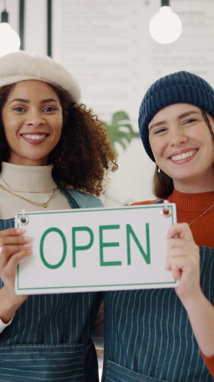 Two Smiling Female Baristas Holding an Open Sign in a Cafe